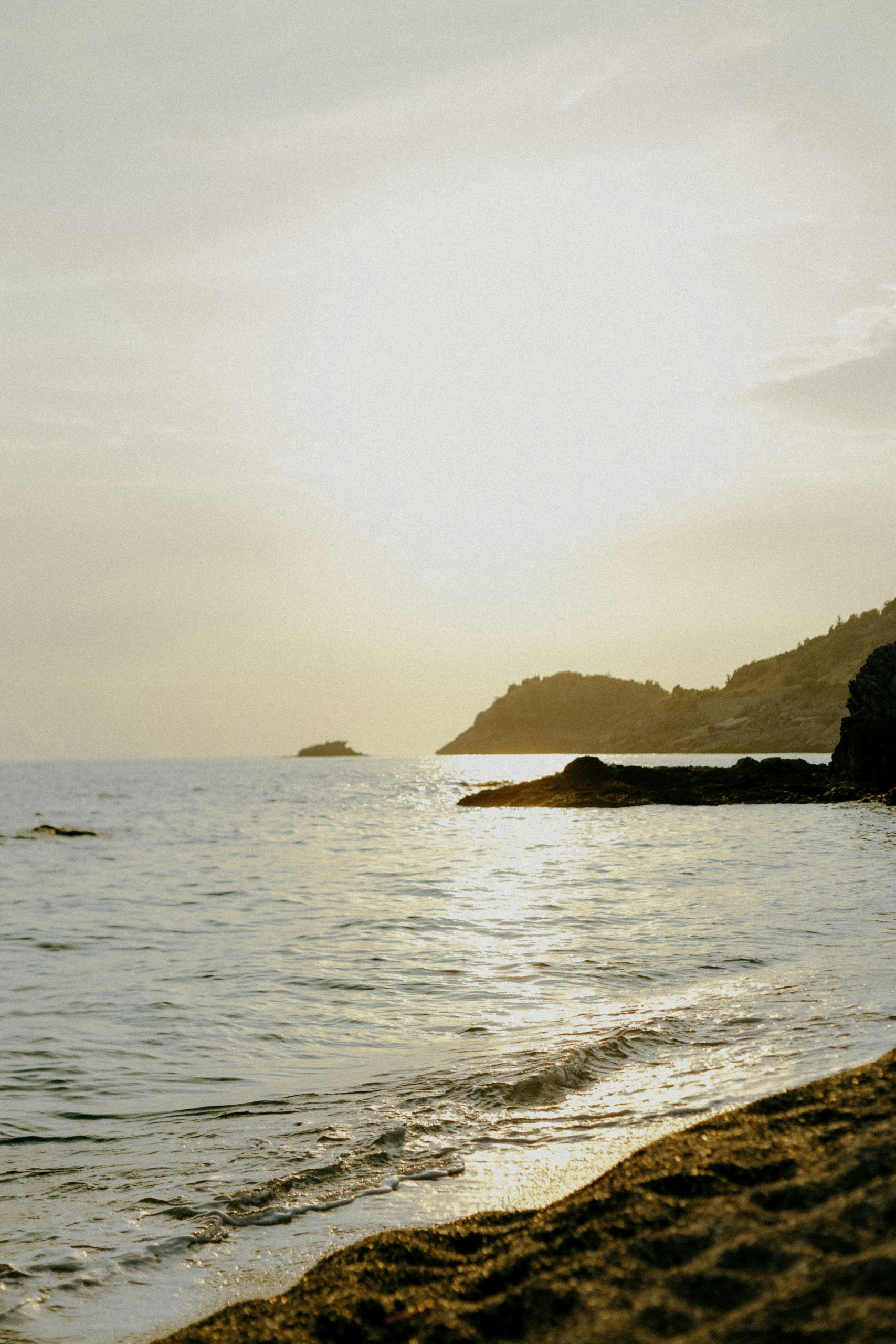 A serene view of the beach and ocean with a golden sunset illuminating the coastline.