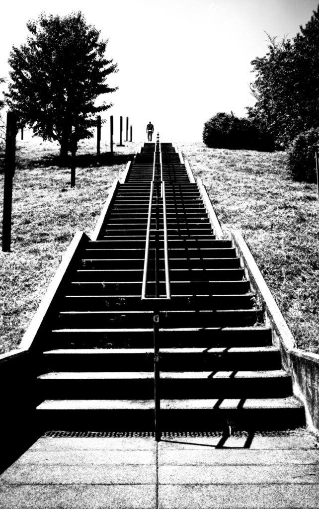 Black and white photo of steep stairs ascending to a bright horizon with a lone figure at the top.