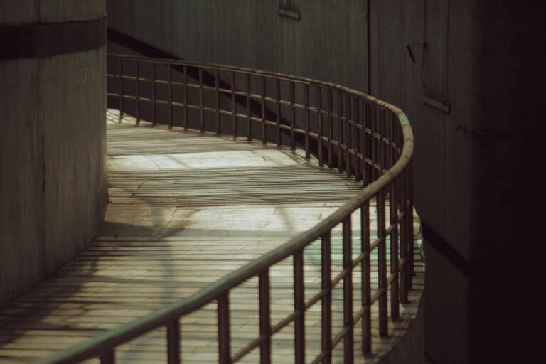 A curved wooden pathway with railings in an industrial urban environment, casting shadows.
