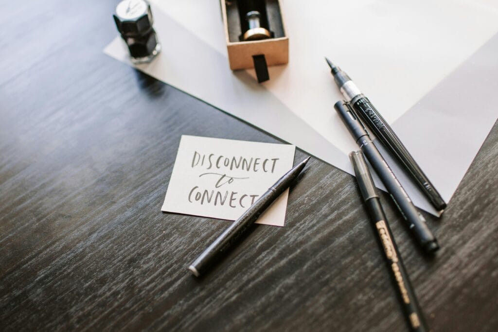 A motivational 'Disconnect to Connect' note surrounded by pens and ink on a wooden desk.